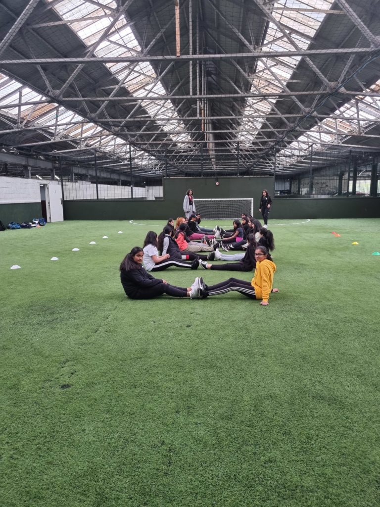Young people on a football pitch stretching on the grass