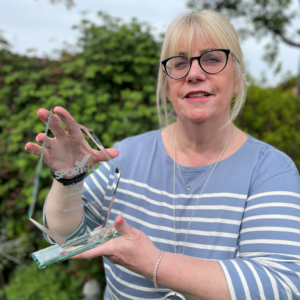 A woman in a blue striped top stands holding her Sported volunteer award in her garden