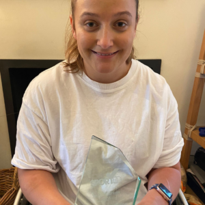 A young woman sits in her wheelchair holding a glass Sported volunteer award