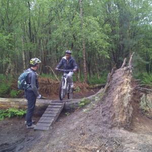 boy on bike doing mountain bike skills with adult watching in a woodland setting