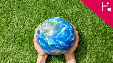hands holding an earth globe size of a football, on a grass background. Red information graphic in corner