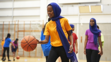 girl wearing blue headscarf playing basket ball in an indoor gym