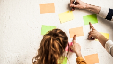 woman and man pointing at post it notes on a wall